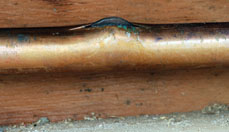 closeup image of a frozen and cracked copper water pipe with ice pushing out of the crack